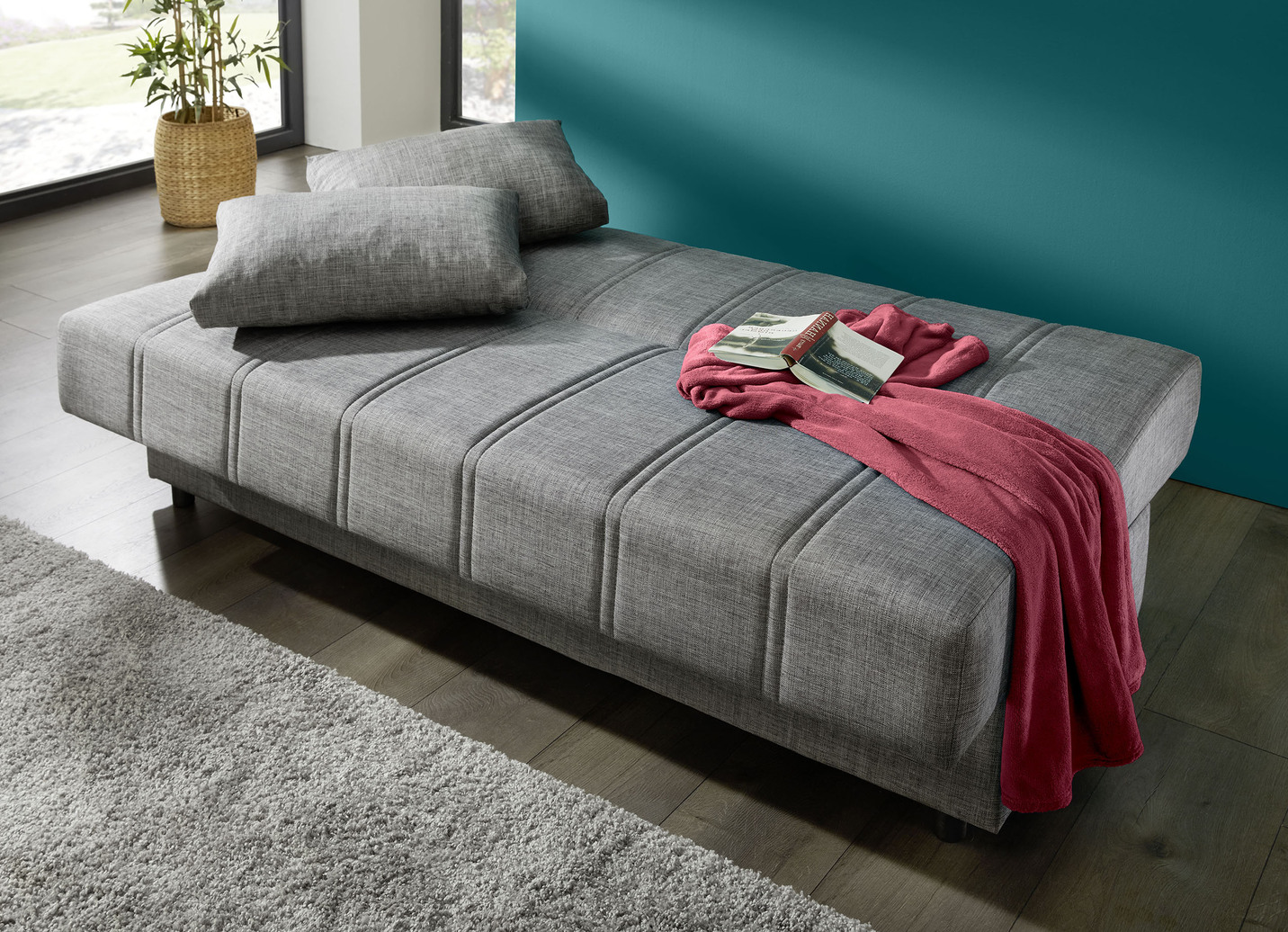 Frei im Raum aufstellbares Schlafsofa mit Dekokissen und Bettkasten